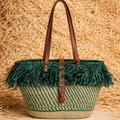 Woven basket with green feather trim and brown leather straps on a straw background