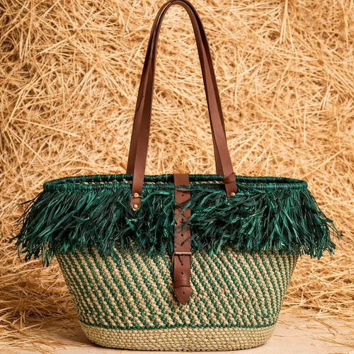 Woven basket with green feather trim and brown leather straps on a straw background